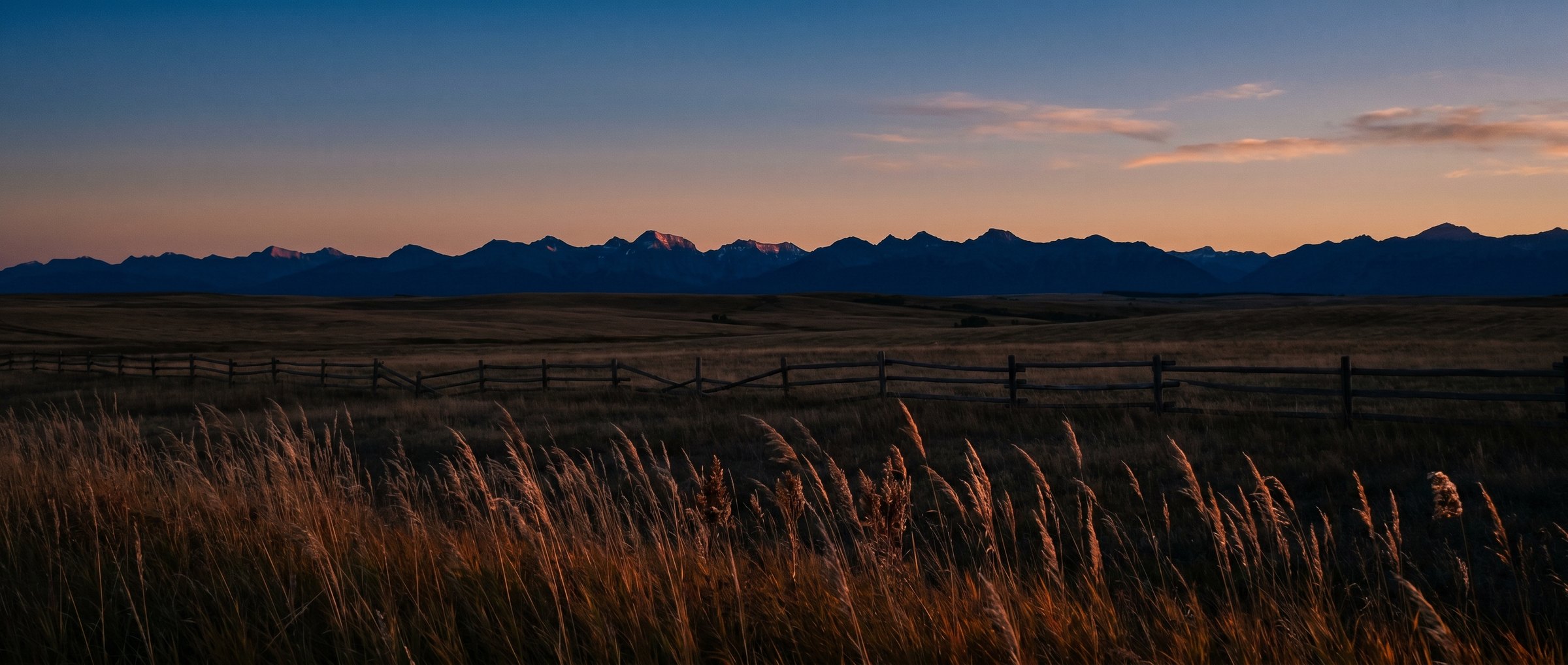 Alberta prairie at dusk with the Canadian Rockies in deep indigo silhouette